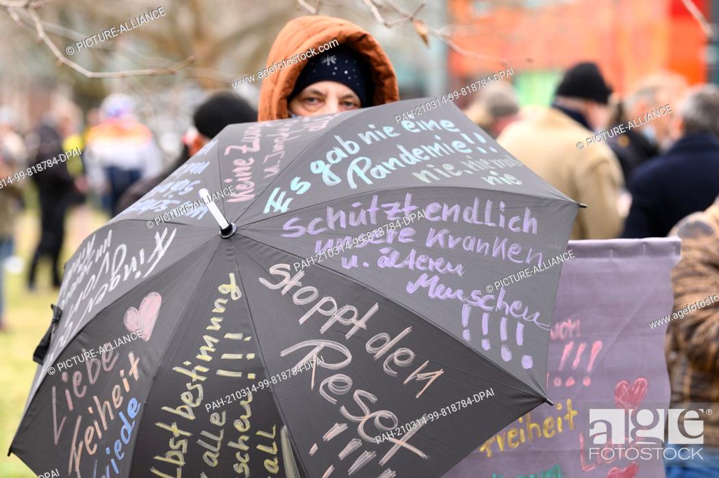 Stock Photo: 13 March 2021, Saxony, Dresden: A woman holds an umbrella with inscriptions such as ""Stop the Reset"" and ""Finally Protect Our Sick and Elderly"" and a banner.