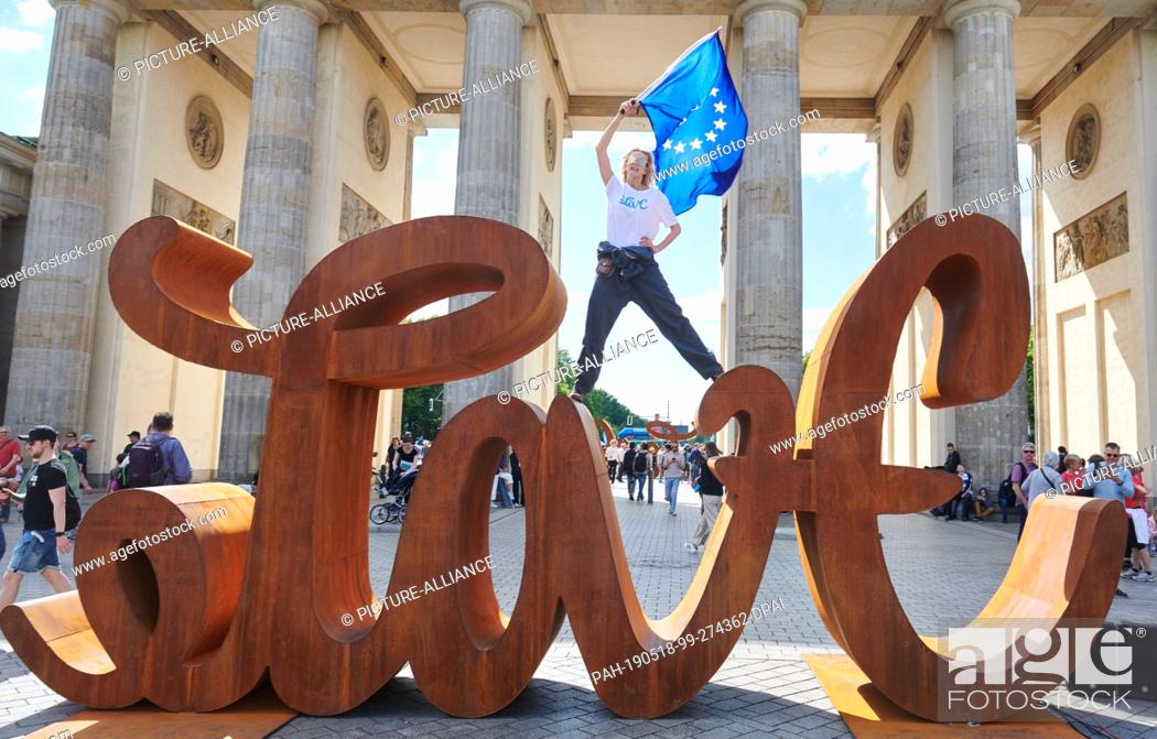 Stock Photo: 18 May 2019, Berlin: The artist Mia Florentine Weiss stands on her sculpture ""Love Hate"" in front of the Brandenburg Gate and waves the European flag.