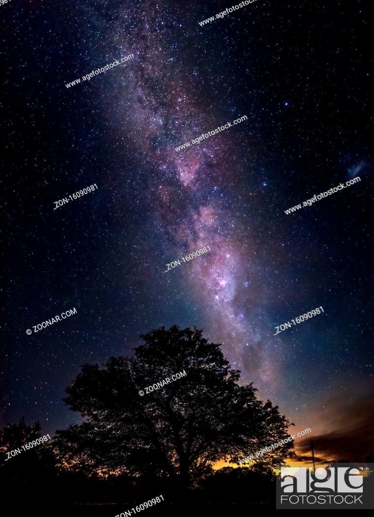 Stock Photo: Amazing night scene of the milky way falling towards the silhouette of a leafy tree showing millions of shiny stars like sand in the sky.