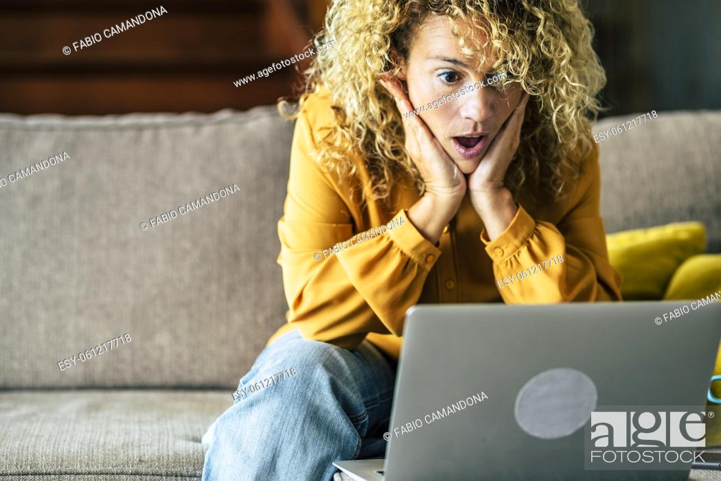 Stock Photo: Happy smiling woman sitting at home on the sofa reading message looking at device screen using computer. Excited female feels satisfied positive emotions took.