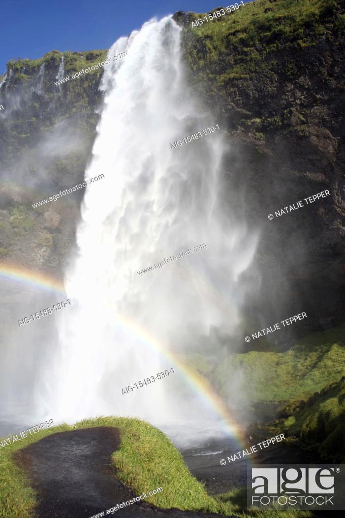 Stock Photo: A stunning landscape of a large waterfall called Seljalandsfoss Waterfall , in Iceland, surrounded by fields and mountains, and crowds, and a rainbow.