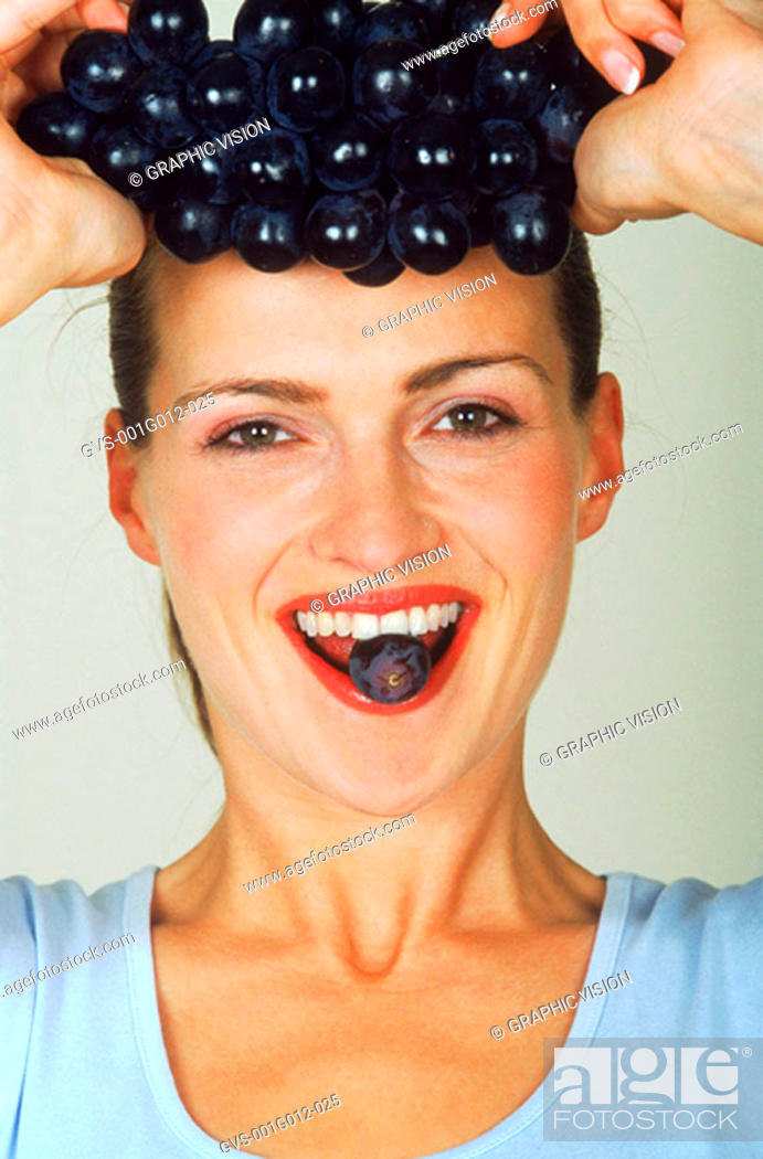 Stock Photo: Portrait of a young woman holding a bunch of grapes above her head.