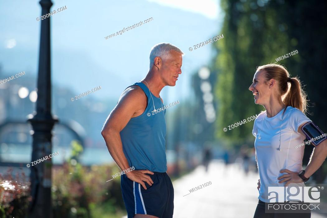 Stock Photo: jogging couple check music playlist on phone and plan route before morning running workout with sunrise in the city and sun flare in background.
