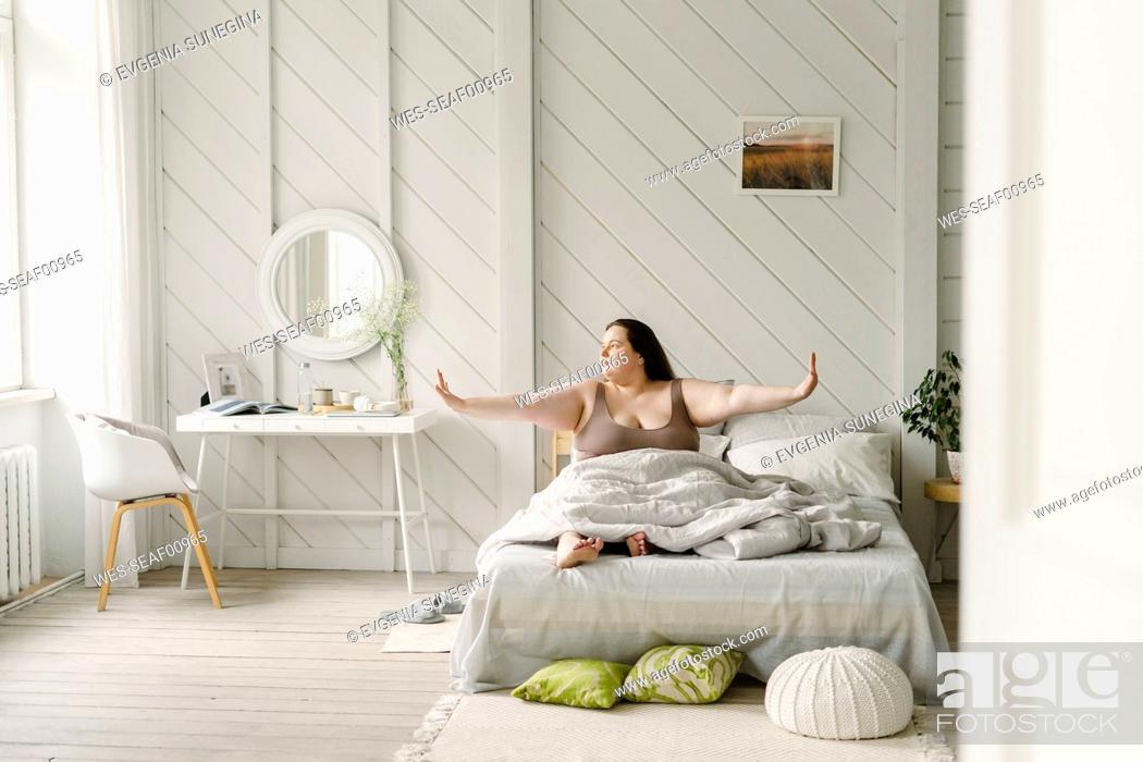 Photo de stock: Woman with arms outstretched sitting on bed at home.