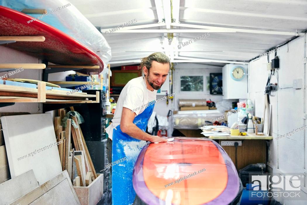Photo de stock: Man polishing and sanding a surfboard in a workshop.