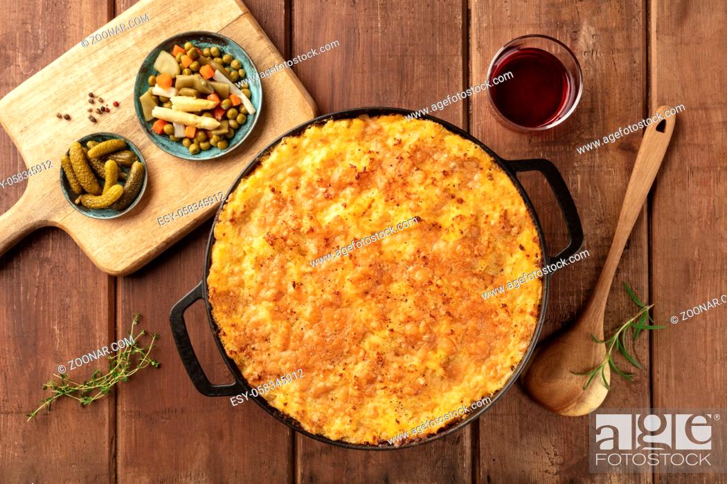Stock Photo: Homemade Shepherd's pie in a cooking pan with pickles and wine, shot from the top on a dark rustic wooden background.