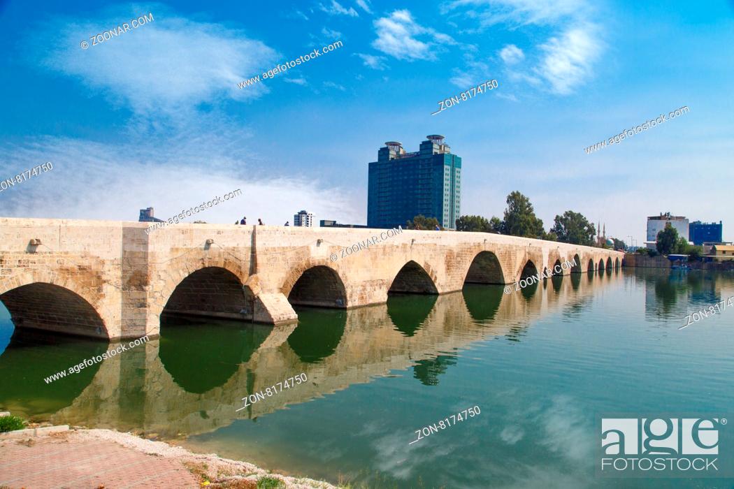 Stock Photo: Side view of historical old stone bridge of Adana on Seyhan river, on cloudy blue sky background.