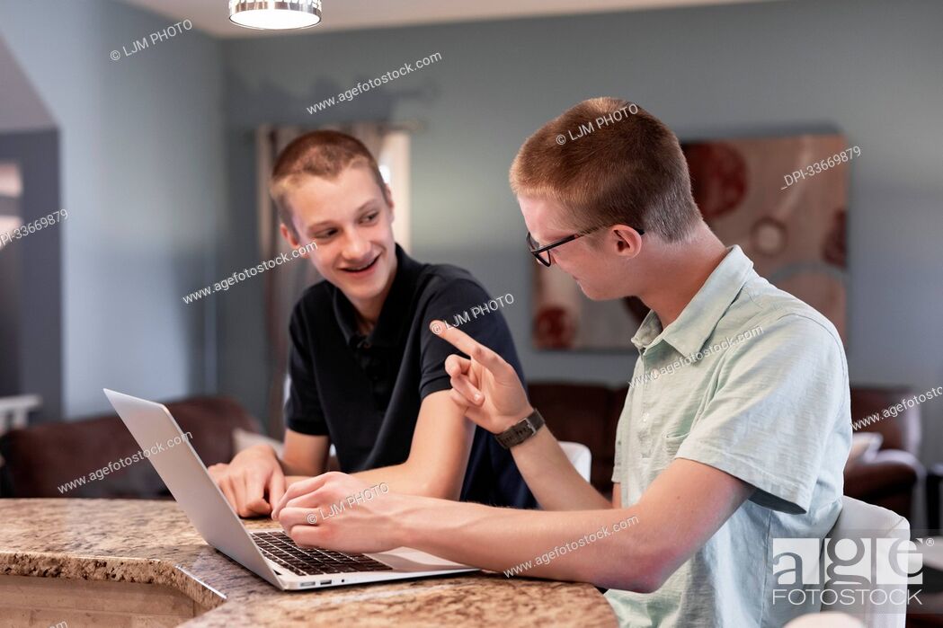 Stock Photo: Young man uses a laptop computer at home with his brother assisting him; Edmonton, Alberta, Canada.