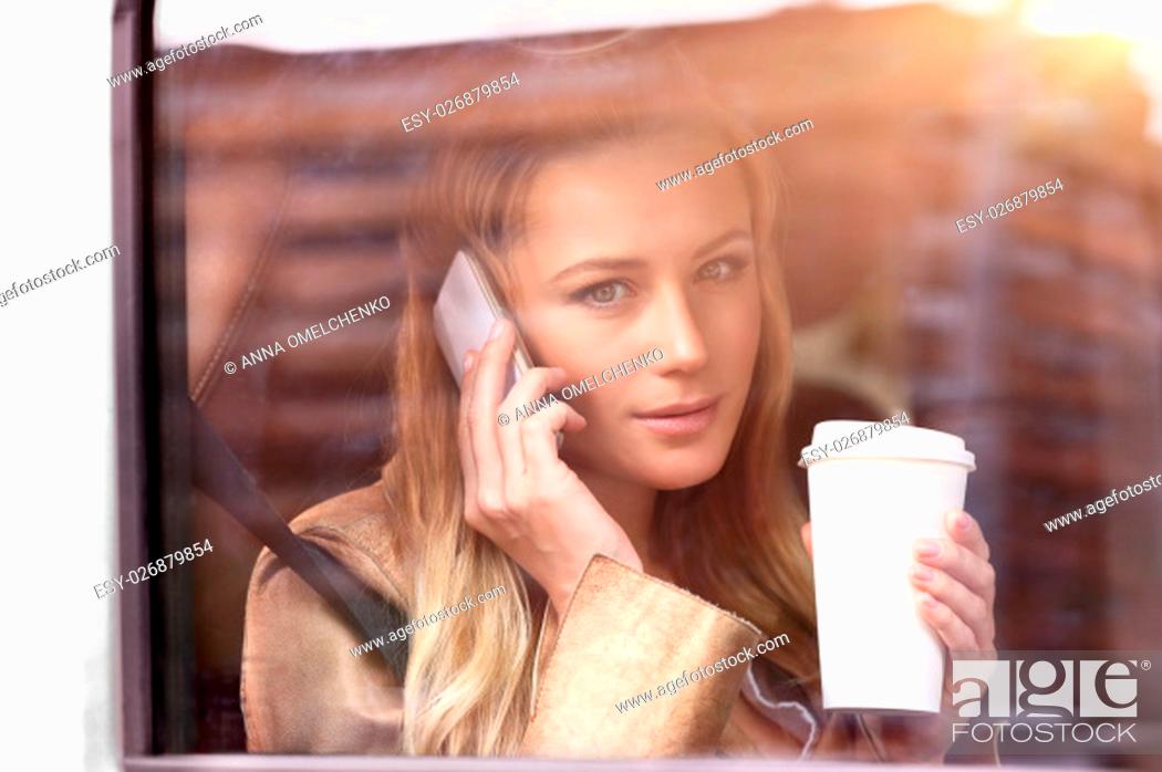 Stock Photo: Portrait of a beautiful business woman sitting in the car with cup of coffee, talking on the phone and looking through car window, going to work.