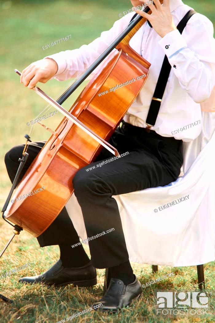 Stock Photo: Young man playing cello outside. Cellist playing classical music on cello.