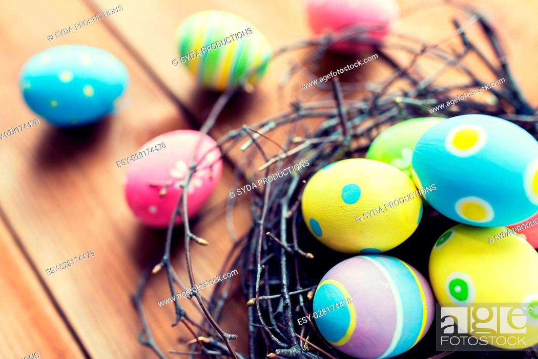 Stock Photo: easter, holidays, tradition and object concept - close up of colored easter eggs in nest on wooden surface.