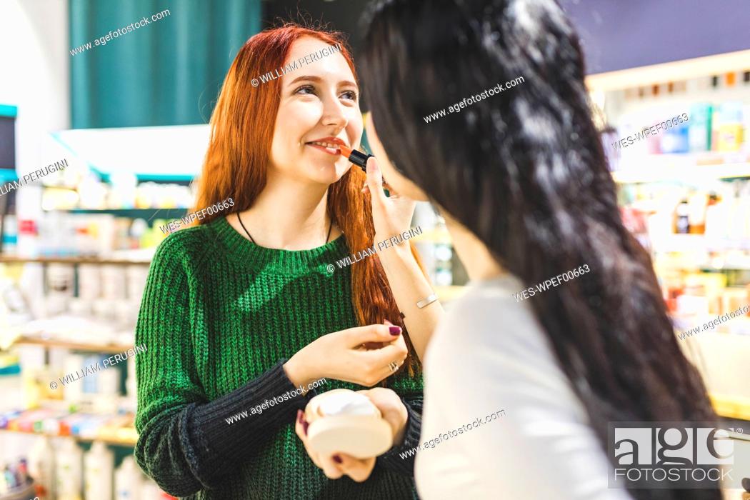 Stock Photo: Two women in a cosmetics shop trying lipstick.