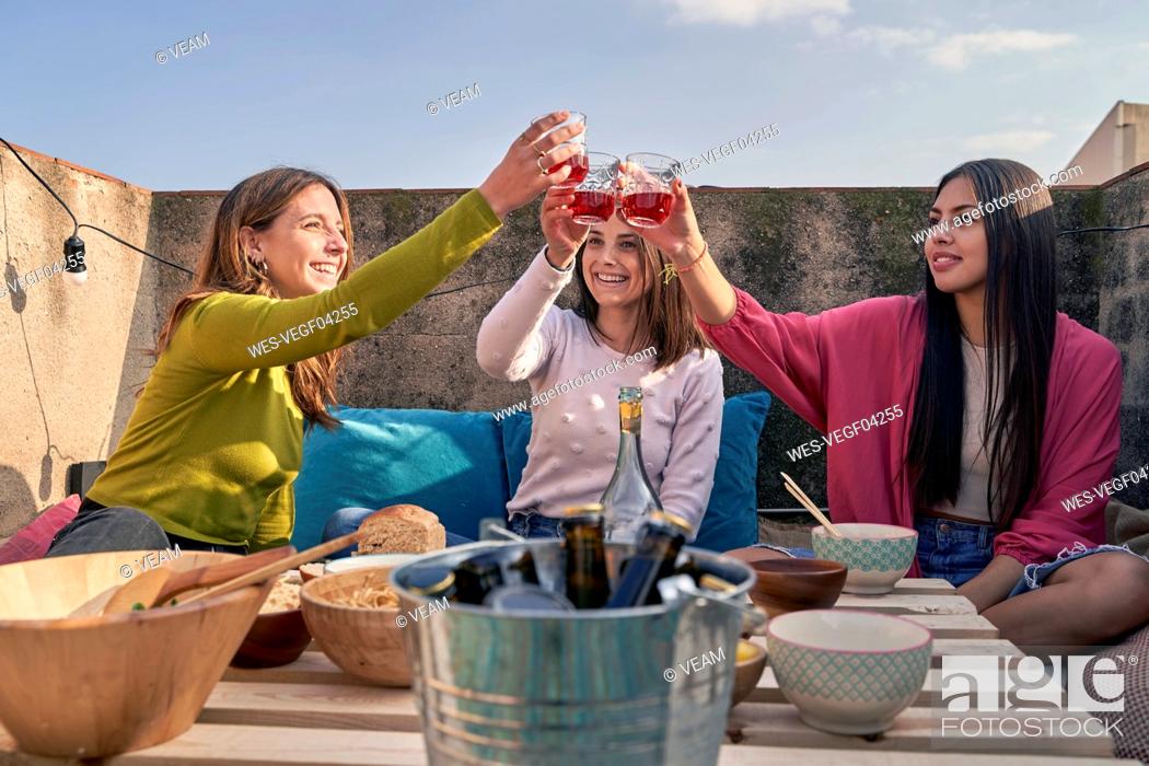 Stock Photo: Female friends toasting wine glass while eating food on rooftop.