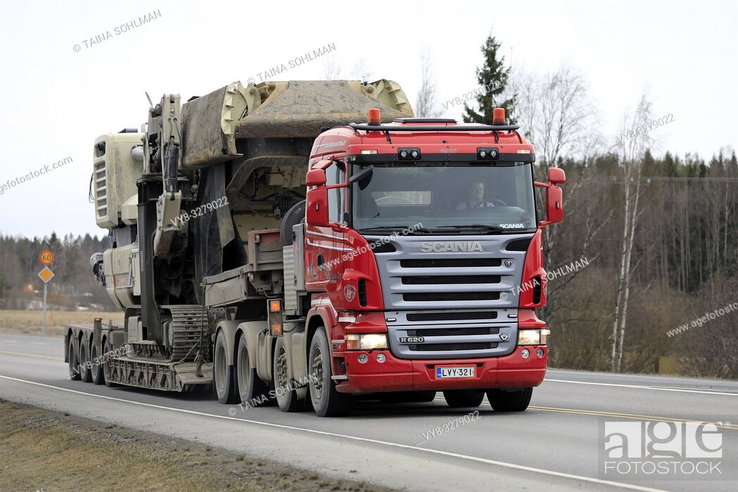 Stock Photo: Forssa, Finland - March 30, 2019: Red Scania R620 semi of Veljekset Makitalo Oy pulls Metso Lokotrack crusher on low loader trailer along highway.