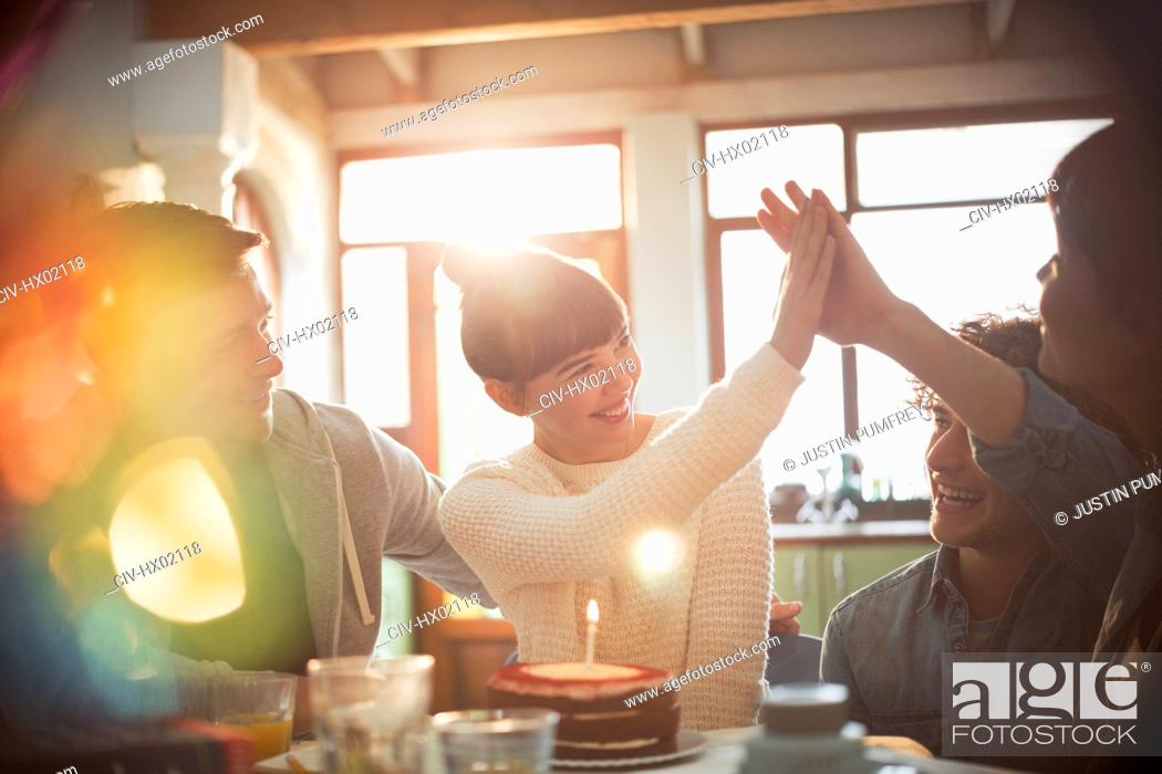 Stock Photo: Young friends celebrating birthday with cake and candle high-fiving.