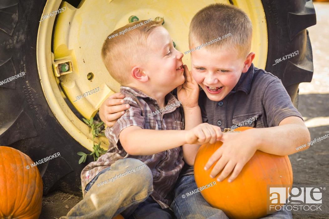 Stock Photo: Two boys sitting against a tractor tire holding pumpkins and whispering secrets in rustic setting.