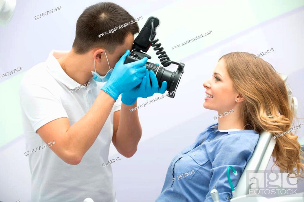 Imagen: Dentist with camera making shots of patients smile after treatment. Special camera with flash ring shadowless.