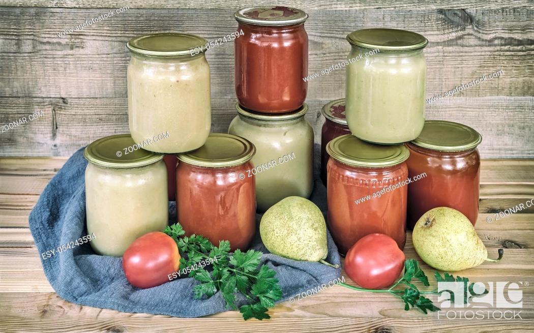 Stock Photo: Pear puree and tomato juice are preserved in glass jars with sealed metal lids. Near lie pears and tomatoes.