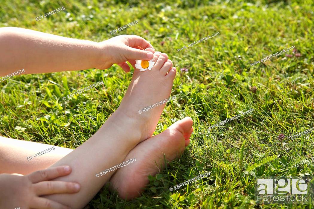 Stock Photo: Small girl sits on green grass and puts a daisy between her toes.