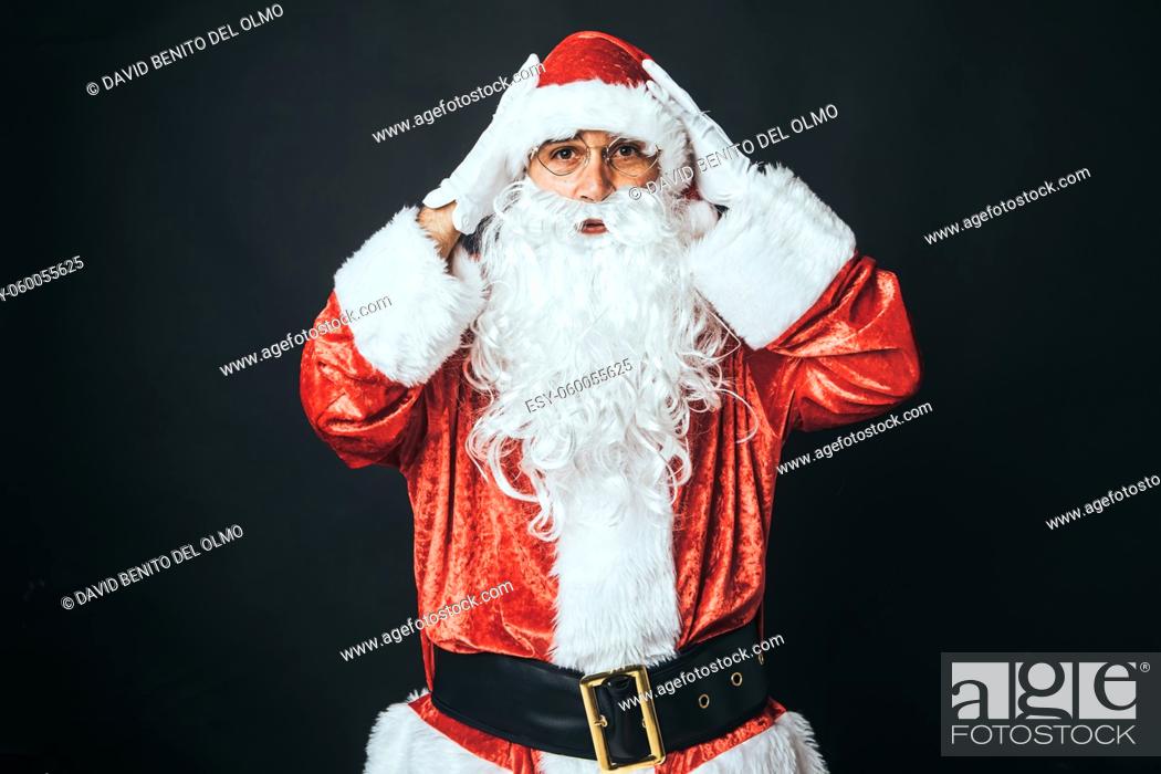 Stock Photo: Man dressed as Santa Claus surprised with hands on head, on black background. Christmas concept, Santa Claus, gifts, celebration.