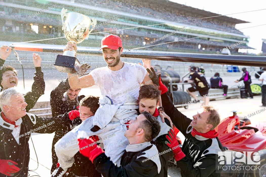 Stock Photo: Formula one racing team carrying driver with trophy on shoulders, celebrating victory on sports track.