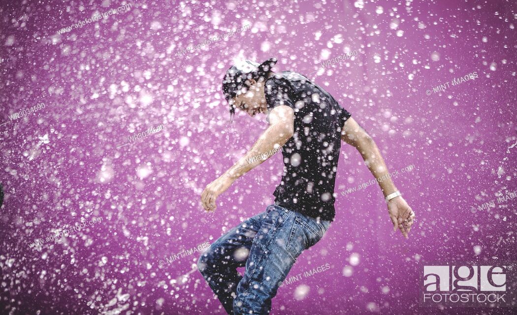 Stock Photo: Young man standing in a shower of water drops.