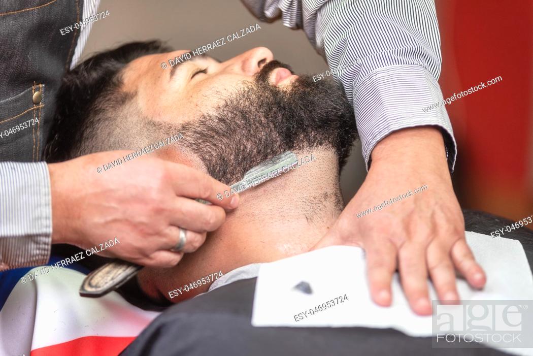 Imagen: Handsome man having a shave with vintage razor at the barbershop .