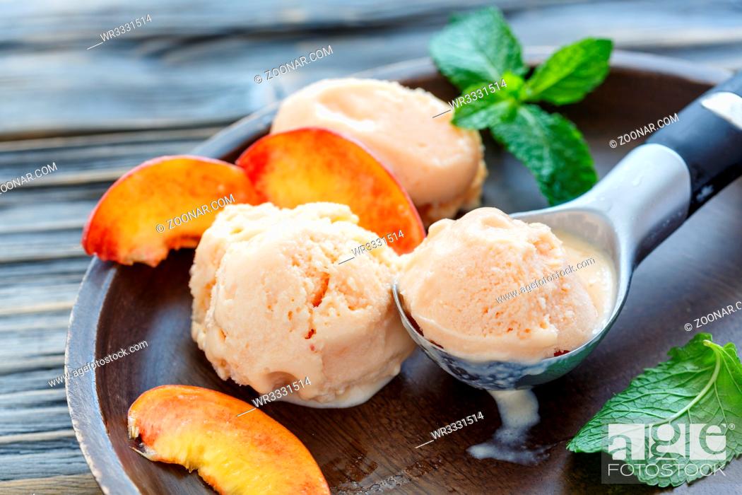 Stock Photo: Homemade peach ice cream in a spoon, slices of peach and mint leaves on wooden plate, selective focus.