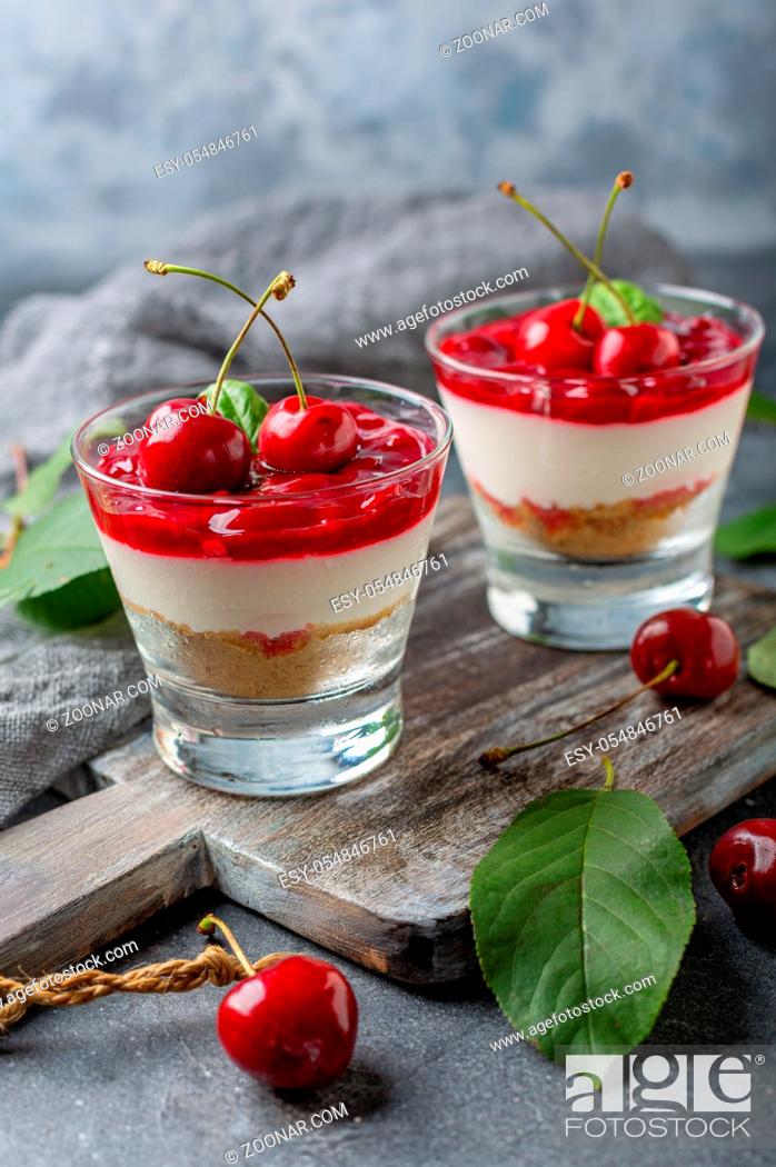 Stock Photo: Cheesecake with cherry jelly in glasses and fresh cherry on a wooden serving board. Textured dark background. Selective focus.