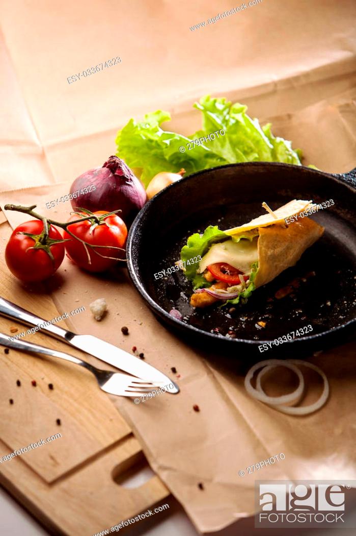 Stock Photo: still life of hot breakfast roll with cheese and vegetables on black cast-iron pan on background of craft paper and wooden board.