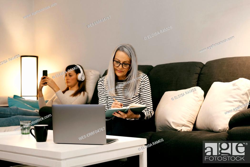 Stock Photo: Mother with laptop writing in book while sitting with daughter in background at home.