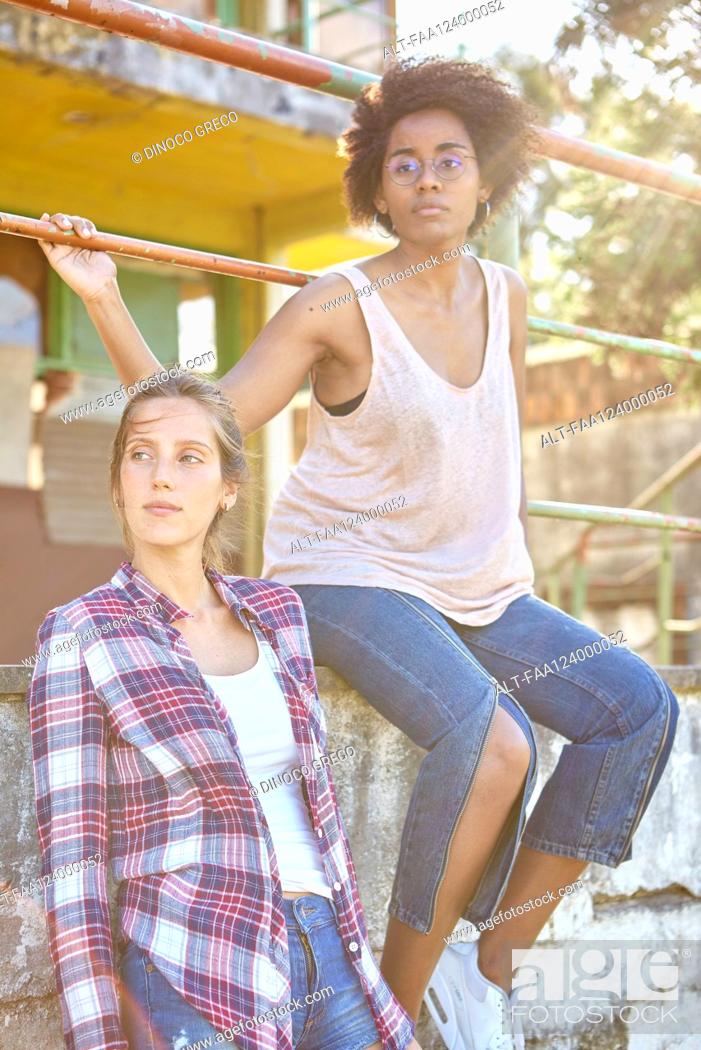 Photo de stock: Young women looking away while sitting on wall.