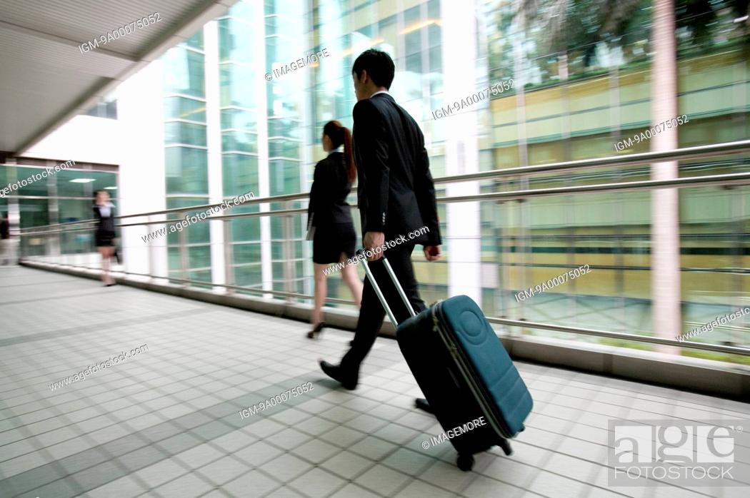 Stock Photo: Businessman walking with rolling suitcase.