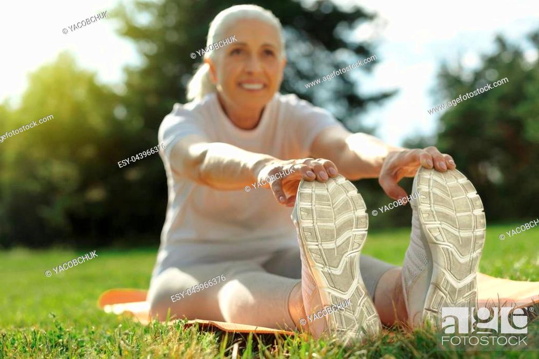 Stock Photo: Feeling much better. Selective focus on feet of a happy elderly lady smiling cheerfully while stretching her back while exercising.