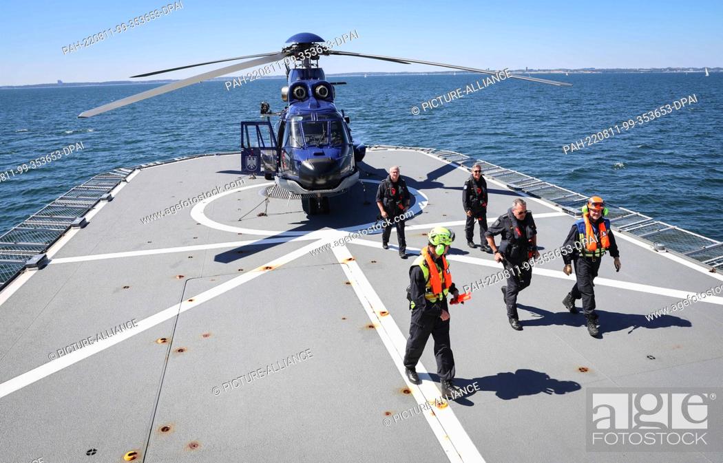 Stock Photo: 11 August 2022, Schleswig-Holstein, Neustadt: The crew of a Super Puma helicopter and crew members walk across the helicopter deck of the ""Potsdam"" response.