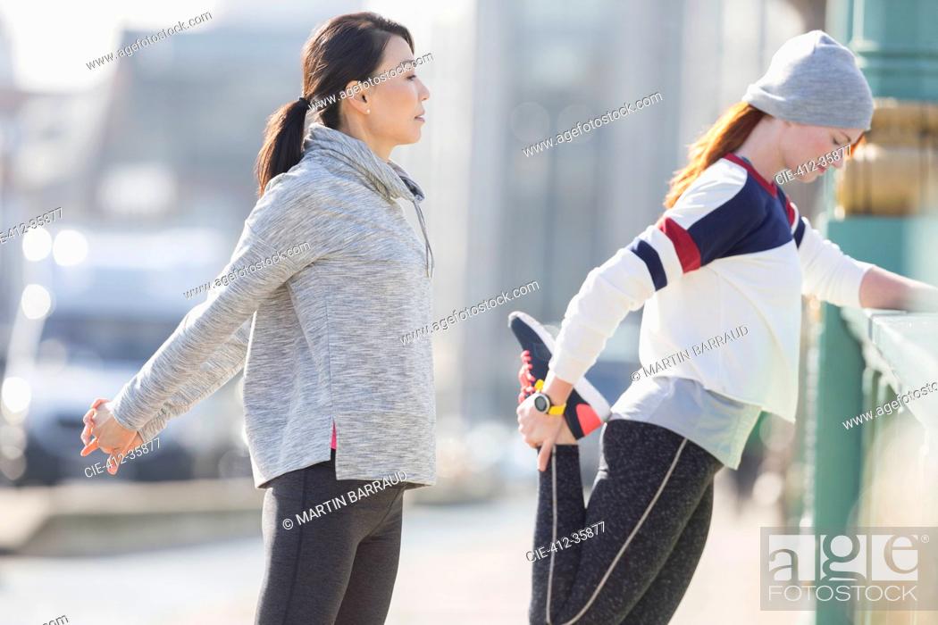 Stock Photo: Female runners stretching on sunny sidewalk.