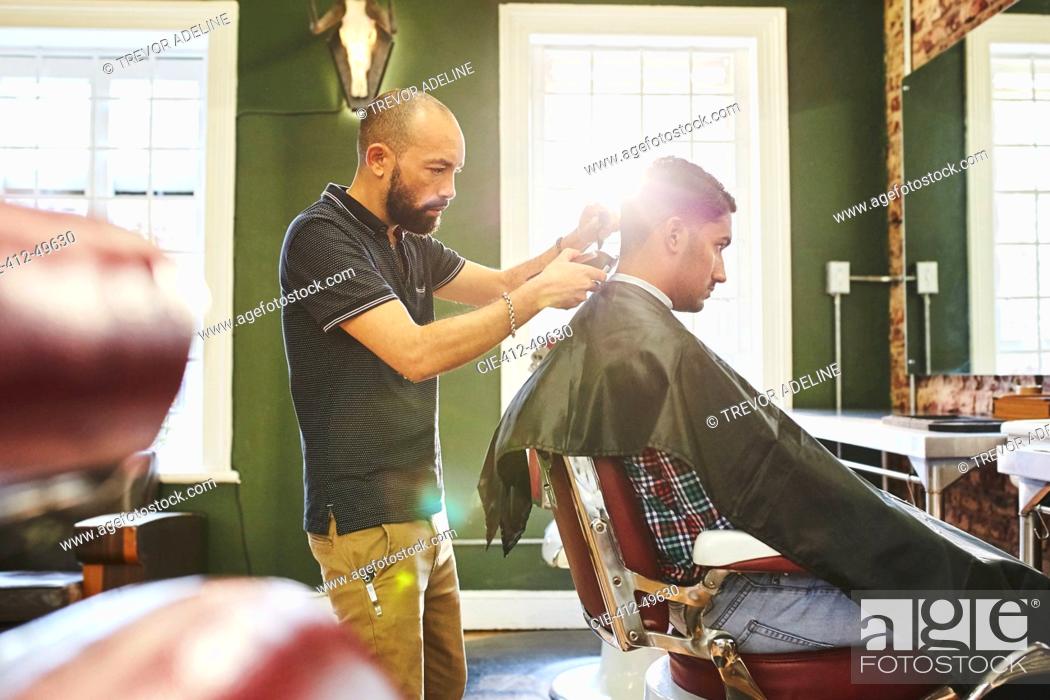 Stock Photo: Focused male barber giving customer a haircut in barbershop.