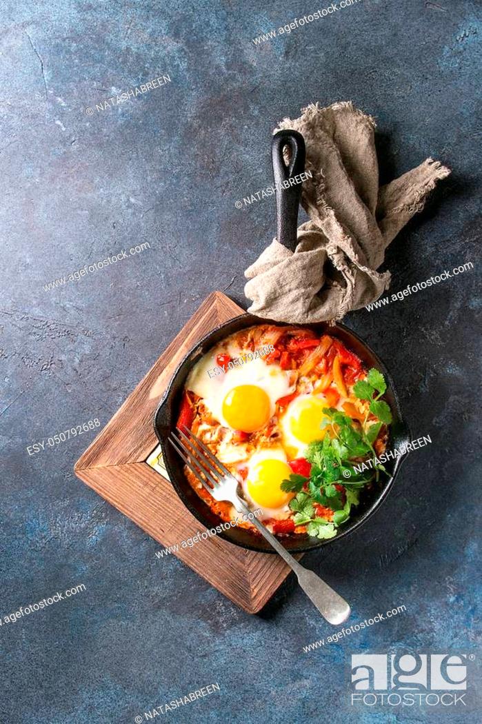 Stock Photo: Traditional Israeli Cuisine dishes Shakshuka. Fried egg with vegetables tomatoes and paprika in cast-iron pan on wooden board with cloth and herbs over blue.