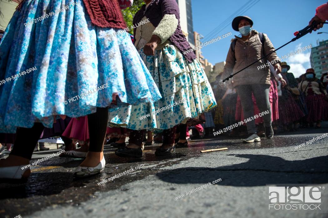 Stock Photo: 10 May 2021, Bolivia, La Paz: A person on the sidelines of a protest sprays demonstrators in traditional dress during a protest to demand better education.