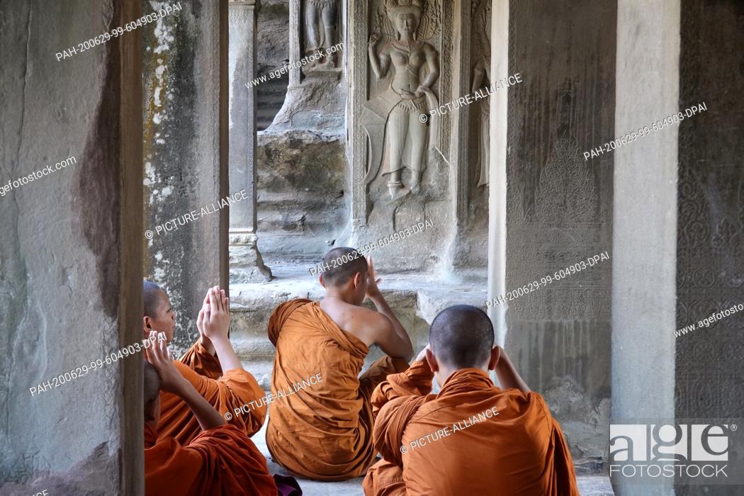 Stock Photo: 23 October 2019, Cambodia, Siem Reab: Monks praying in an orange cape..in the main temple Angkor Wat. King Suryavarman had the temple.