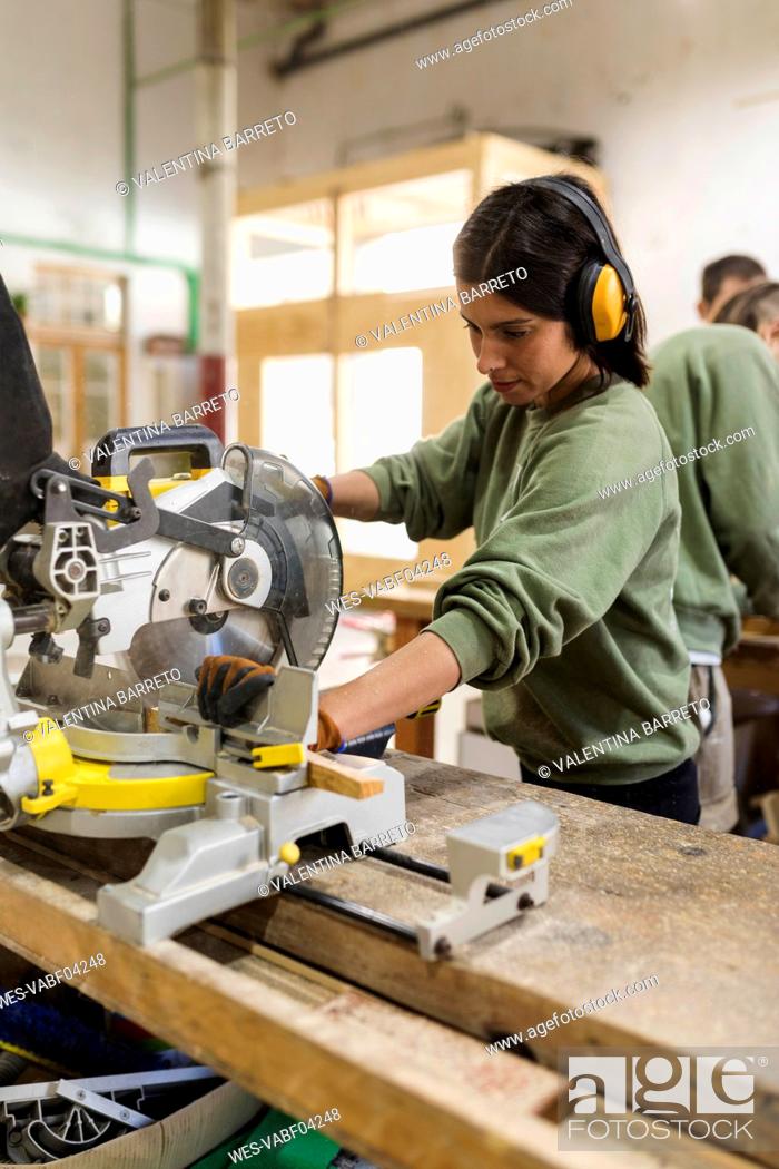 Stock Photo: Female carpenter with ear muff using woodworking equipment at workbench in industry.