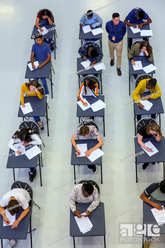 Stock Photo: High school teacher supervising students taking exam at desks.