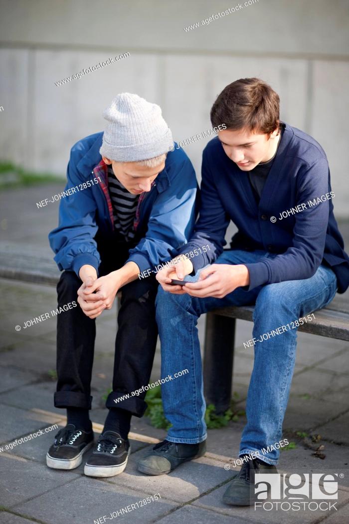 Stock Photo: Two teenage boys sitting on bench with mobile phone.