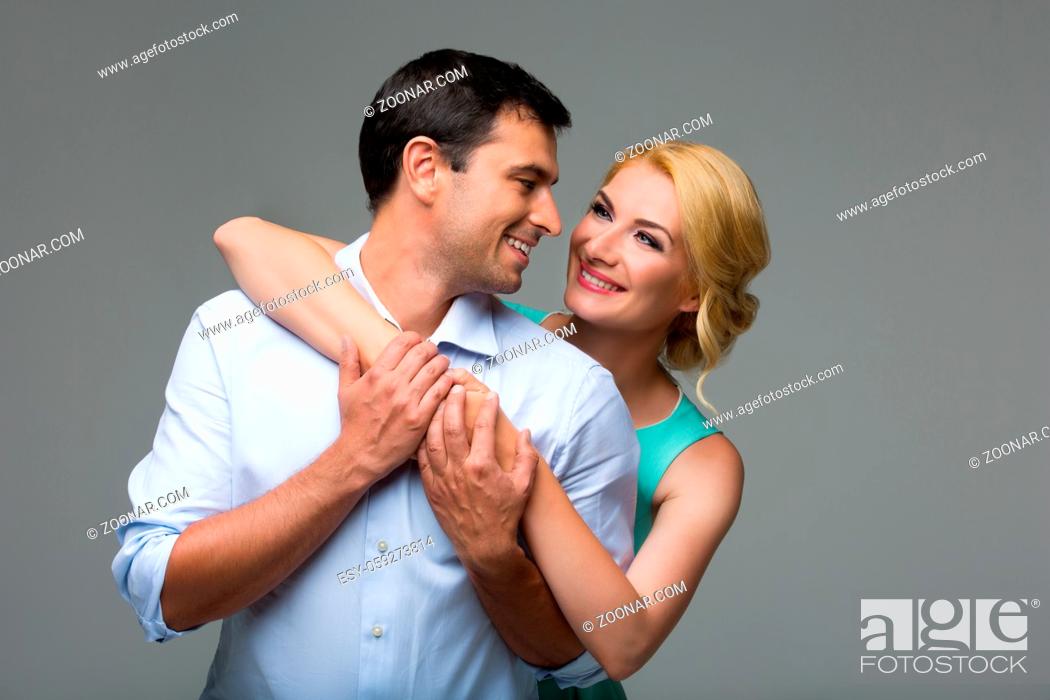 Stock Photo: Beautiful young couple hugging. Blond woman in mint dress and handsome man in shirt and trousers standing on grey background. Valentine's day concept.