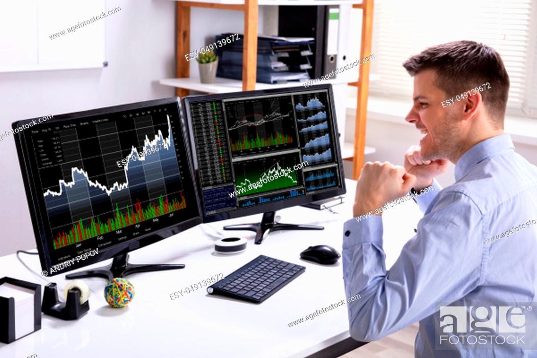 Stock Photo: Excited Young Male Stock Market Broker Looking At Graph On Computer At Workplace.