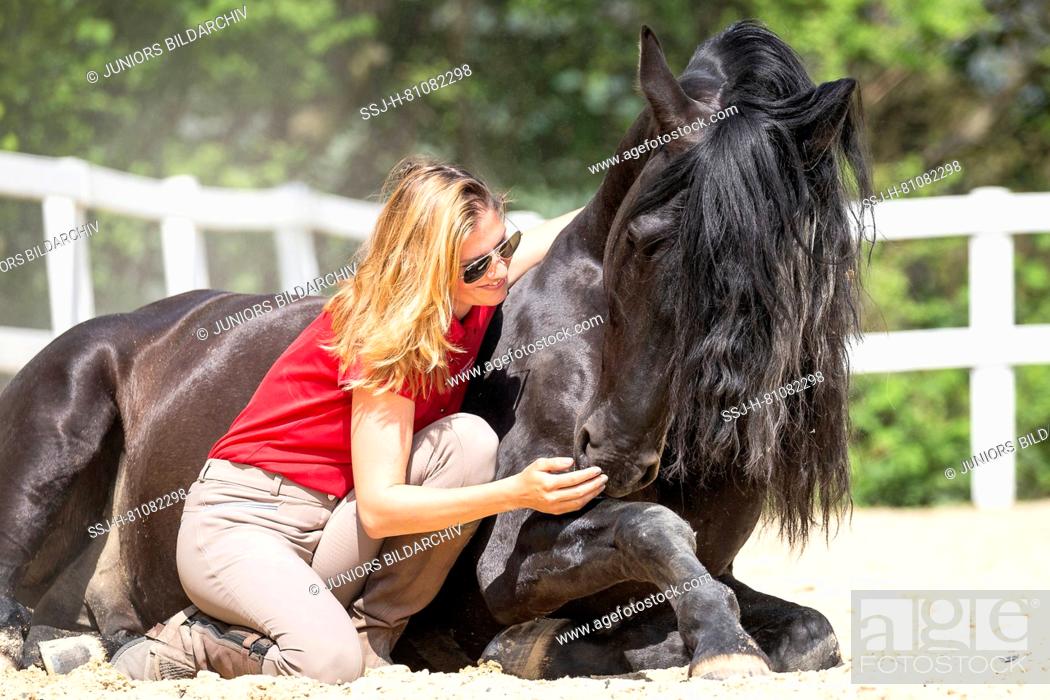 Imagen: Pure Spanish Horse, Andalusian. Woman smooching with black stallion, lying on a riding place. Germany.