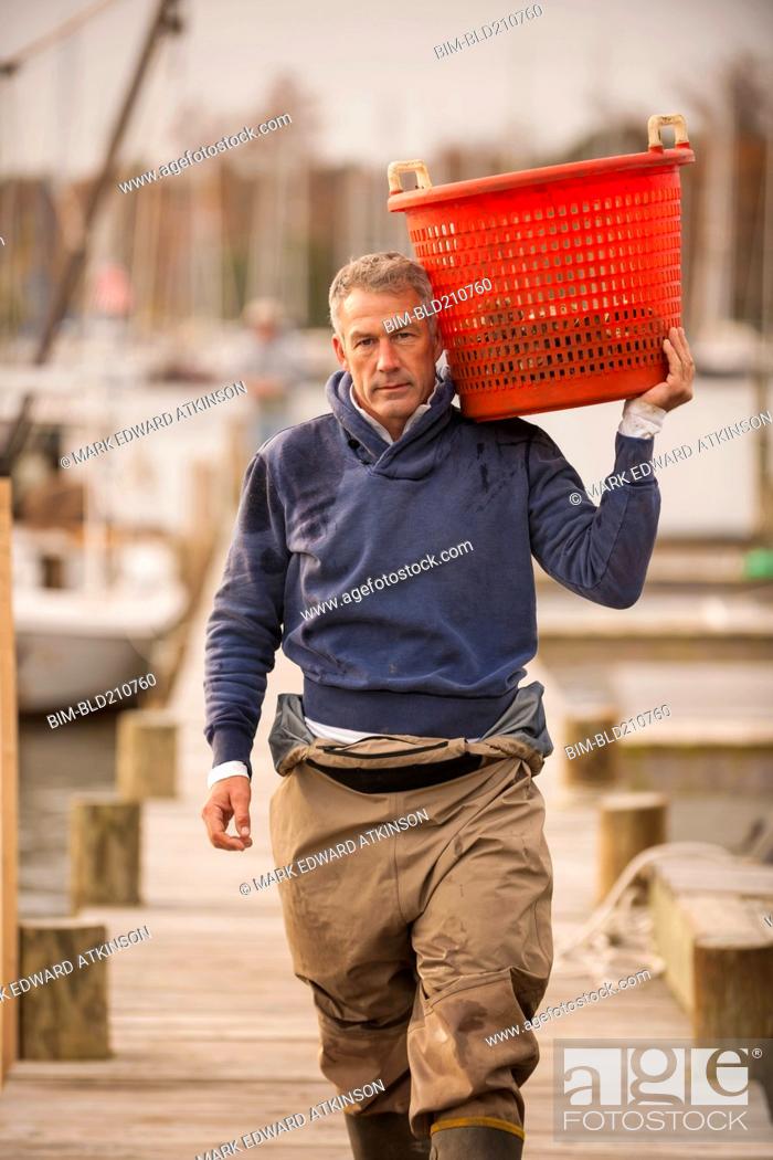 Stock Photo: Caucasian fisherman carrying basket on dock.