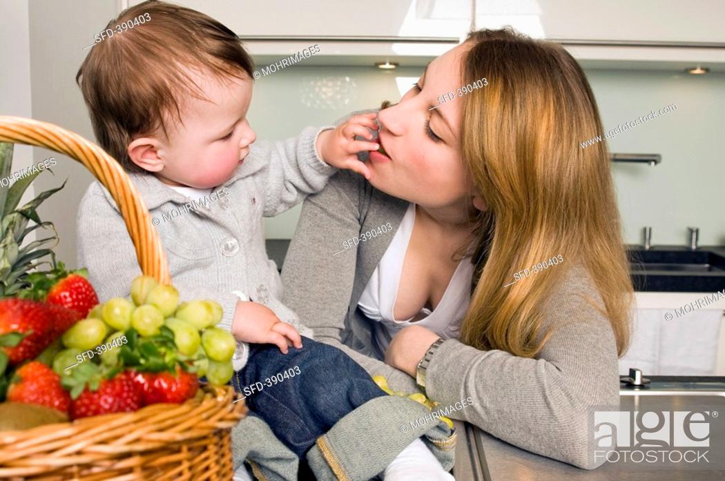 Stock Photo: Toddler with mother beside a basket of fruit.