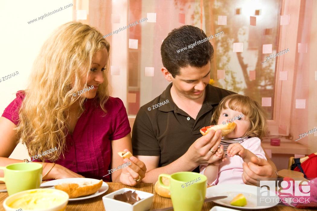 Stock Photo: Junges Ehepaar sitzt am Frühstückstisch und füttert ihr Baby.