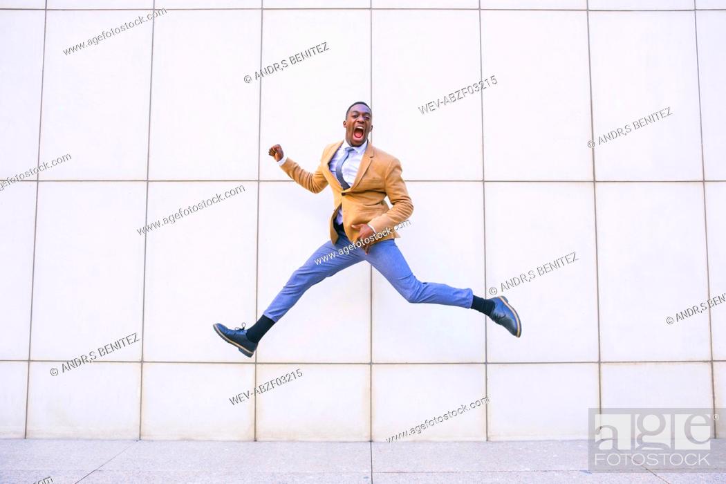 Stock Photo: Young businessman jumping and shouting in front of a wall.